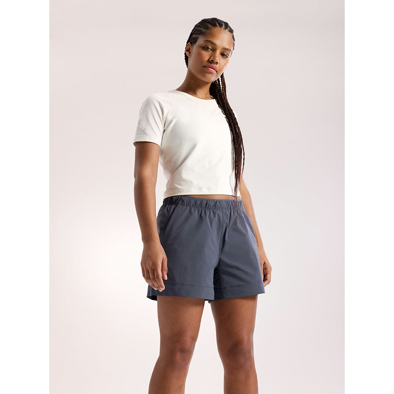 Woman wearing a white crop top and gray shorts on a light pink background