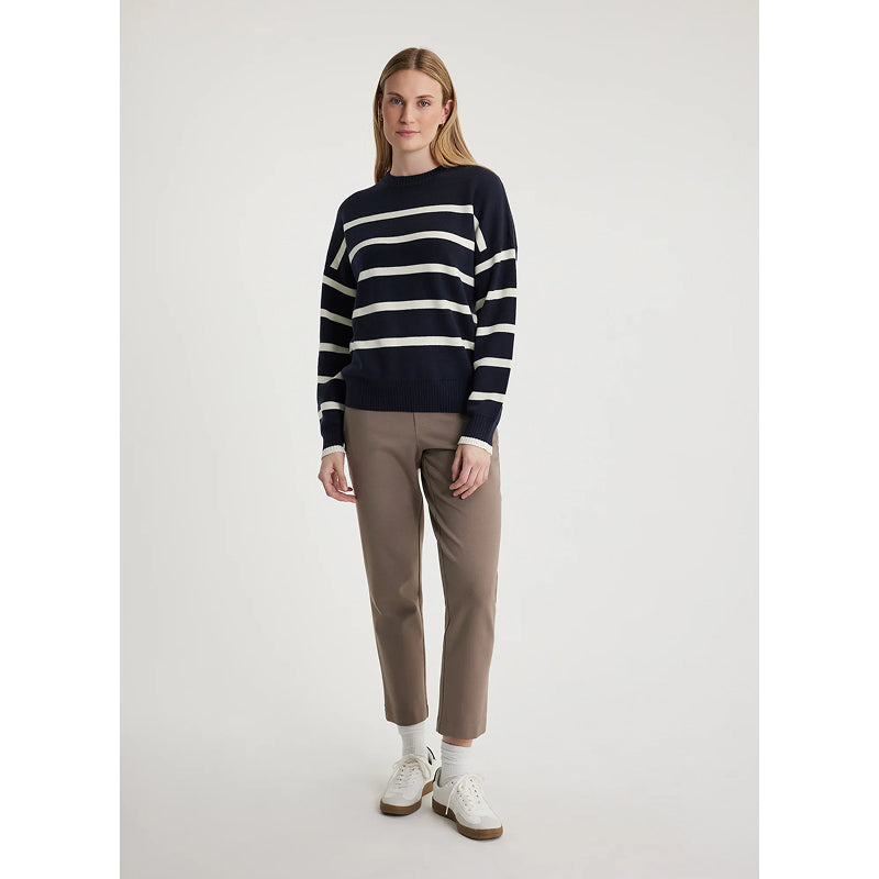 Woman wearing a navy and white striped sweater with beige pants on a light gray background