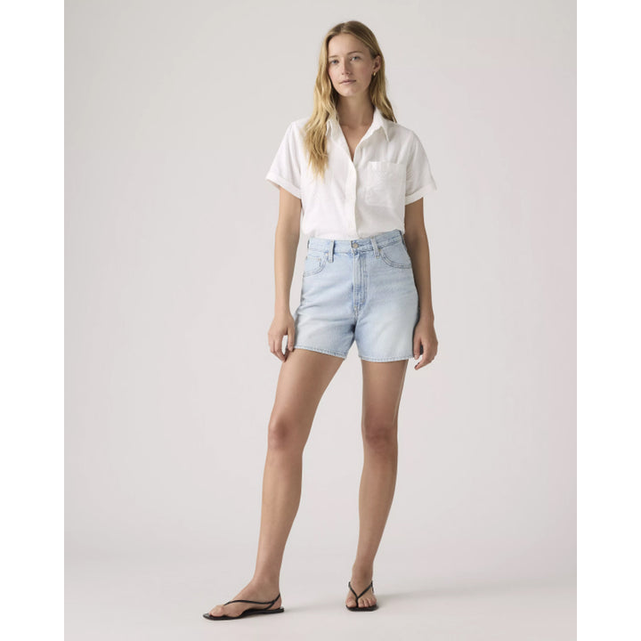 Woman wearing a white shirt and light blue denim shorts on a plain background