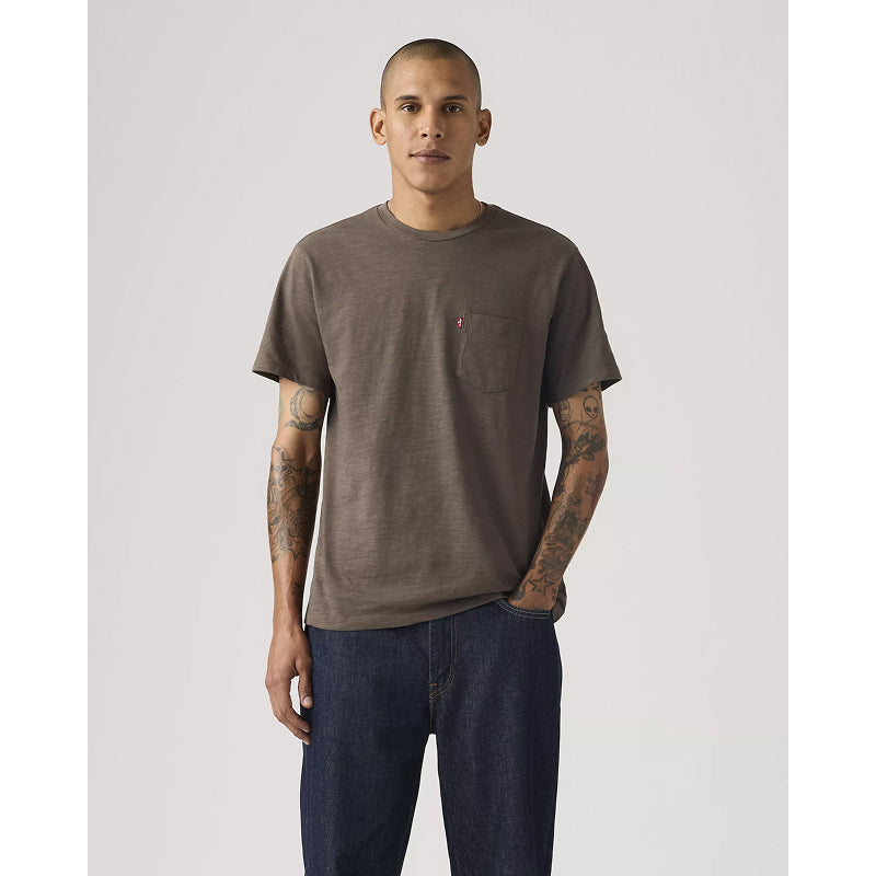 Man wearing a brown t-shirt and dark jeans on a plain background