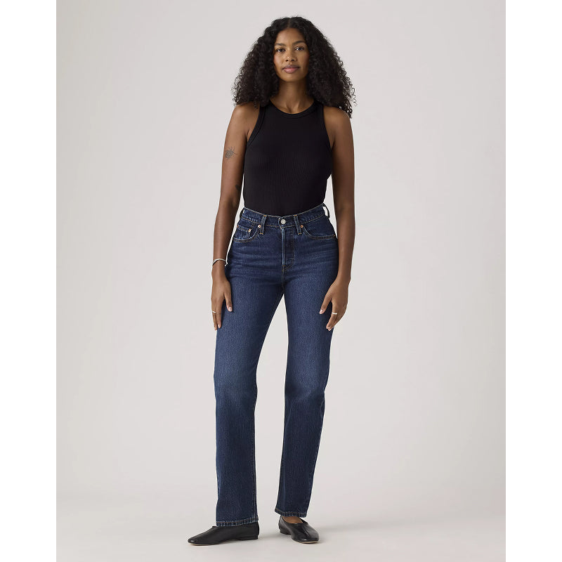 Woman wearing blue jeans and a black top on a plain background