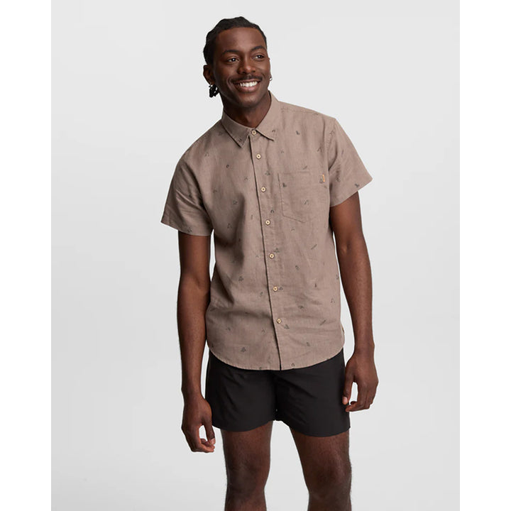 Man wearing a beige short-sleeve shirt and black shorts on a light gray background