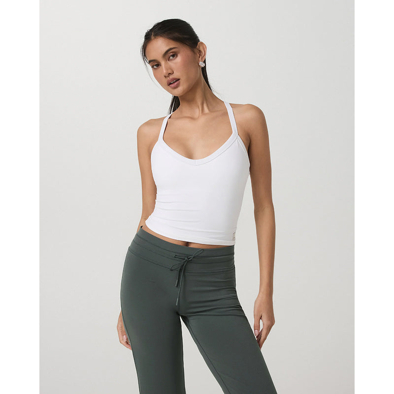 Woman wearing a white tank top and green leggings on a plain background